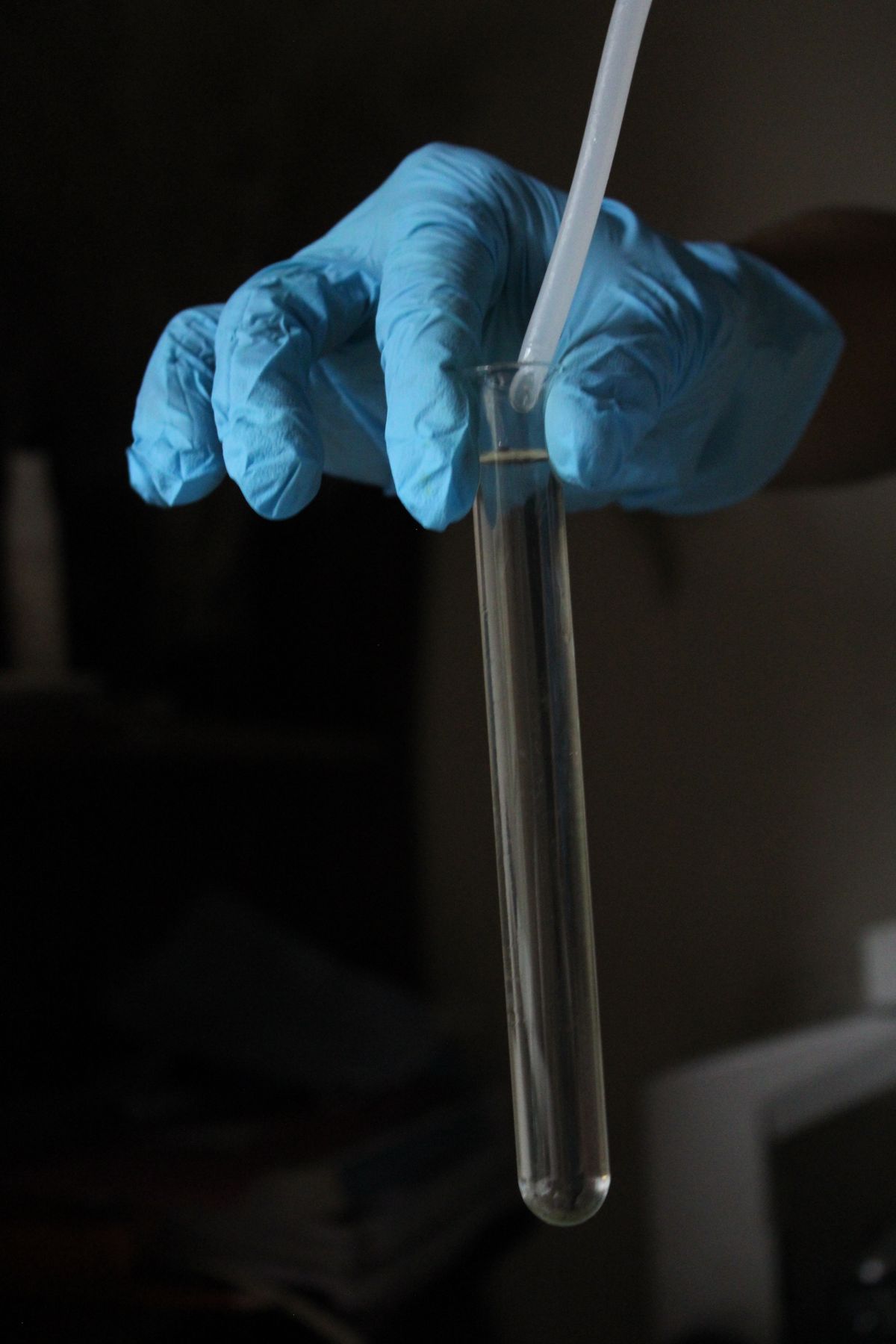 Gloved hand holding a clear sample tube in a darkened laboratory, the paired-sample discipline a hardness check depends on