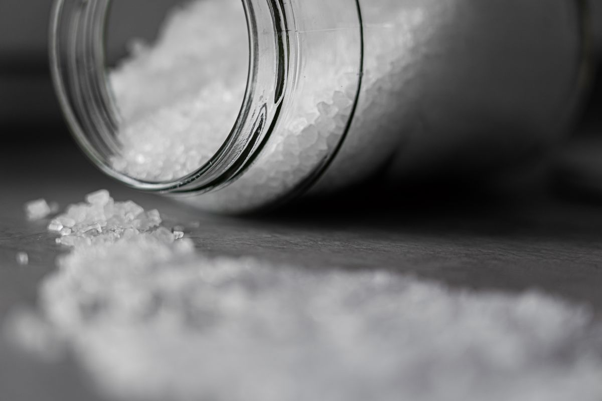 Coarse white salt crystals spilling from a glass jar, the regeneration salt whose annual use scales with hardness in grains per gallon
