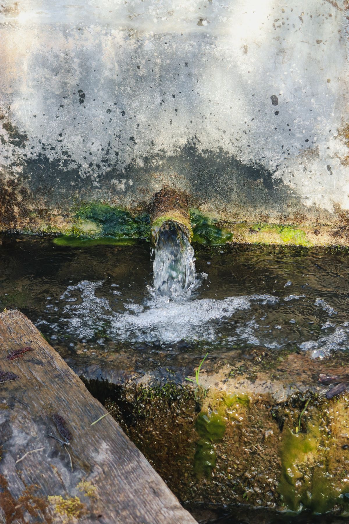 Water pouring from a pipe outlet into a concrete basin below through open air, illustrating the visible gap a softener drain line needs between its end and the receiving drain
