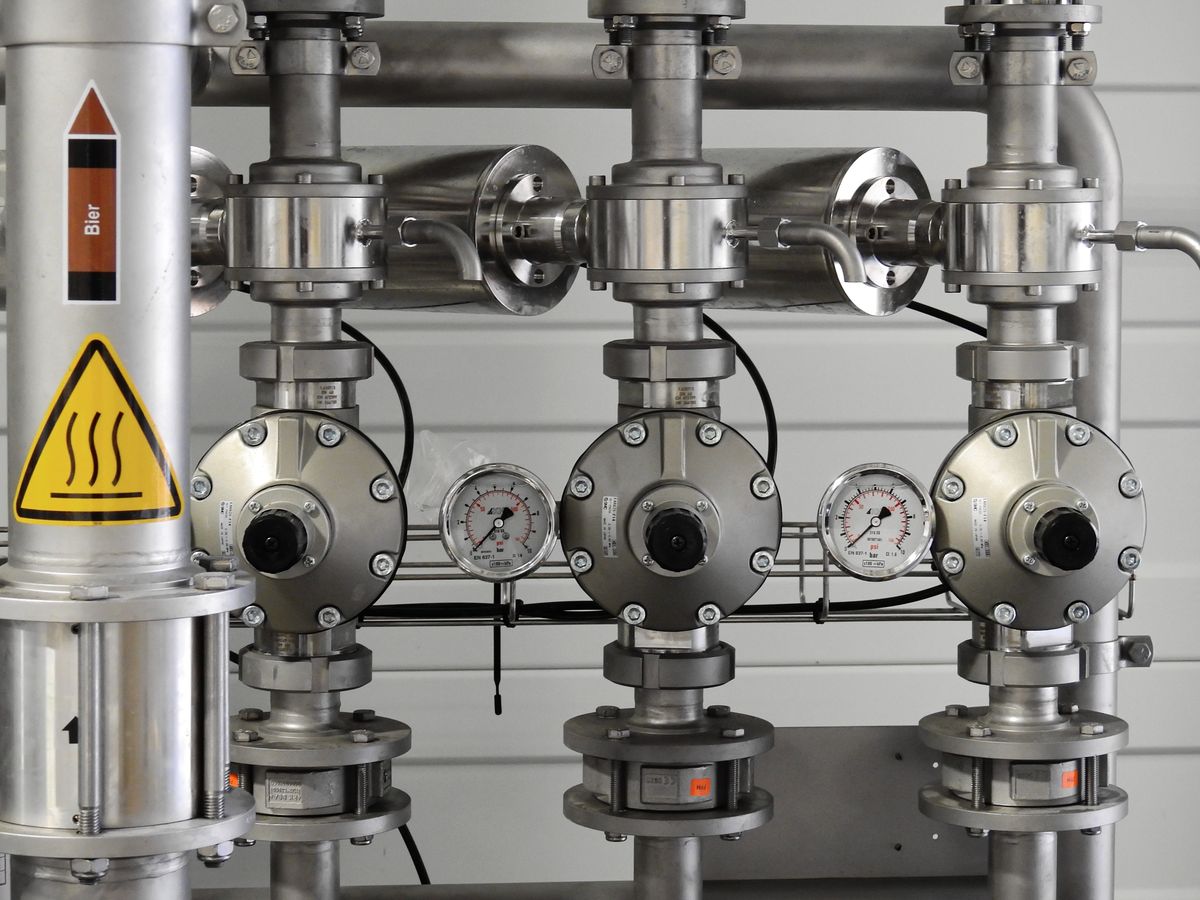 Close-up of stainless steel pipes fitted with pressure gauges in an industrial plant, the kind of rigid pipework in which a sudden valve closure sends a pressure spike