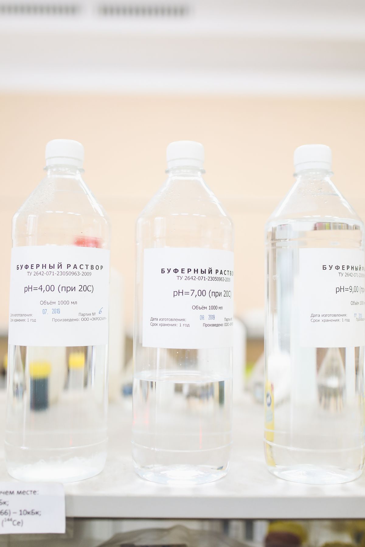 Bottles of pH 4, 7 and 9 buffer solution lined up on a laboratory bench, used to calibrate a pH meter before testing acidic well water