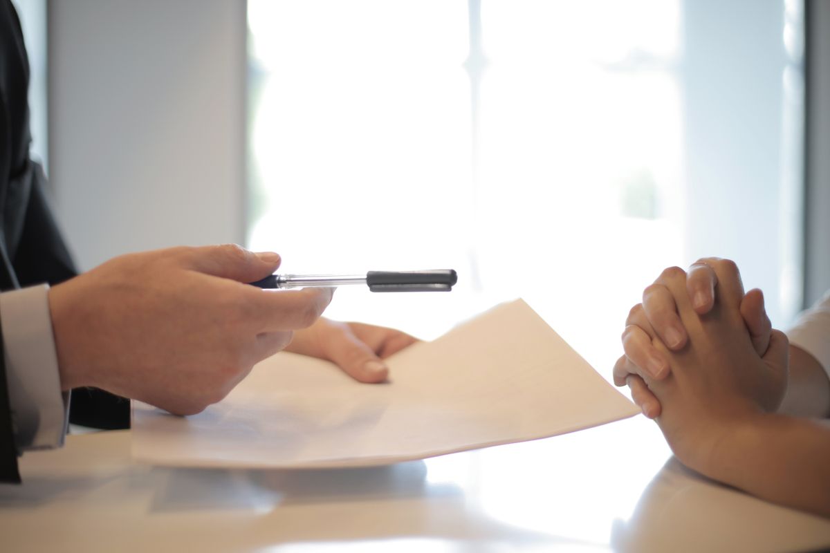 Salesperson holding out a pen and a printed contract to a customer at a table, the point in a Culligan or RainSoft visit to ask for the total cost first