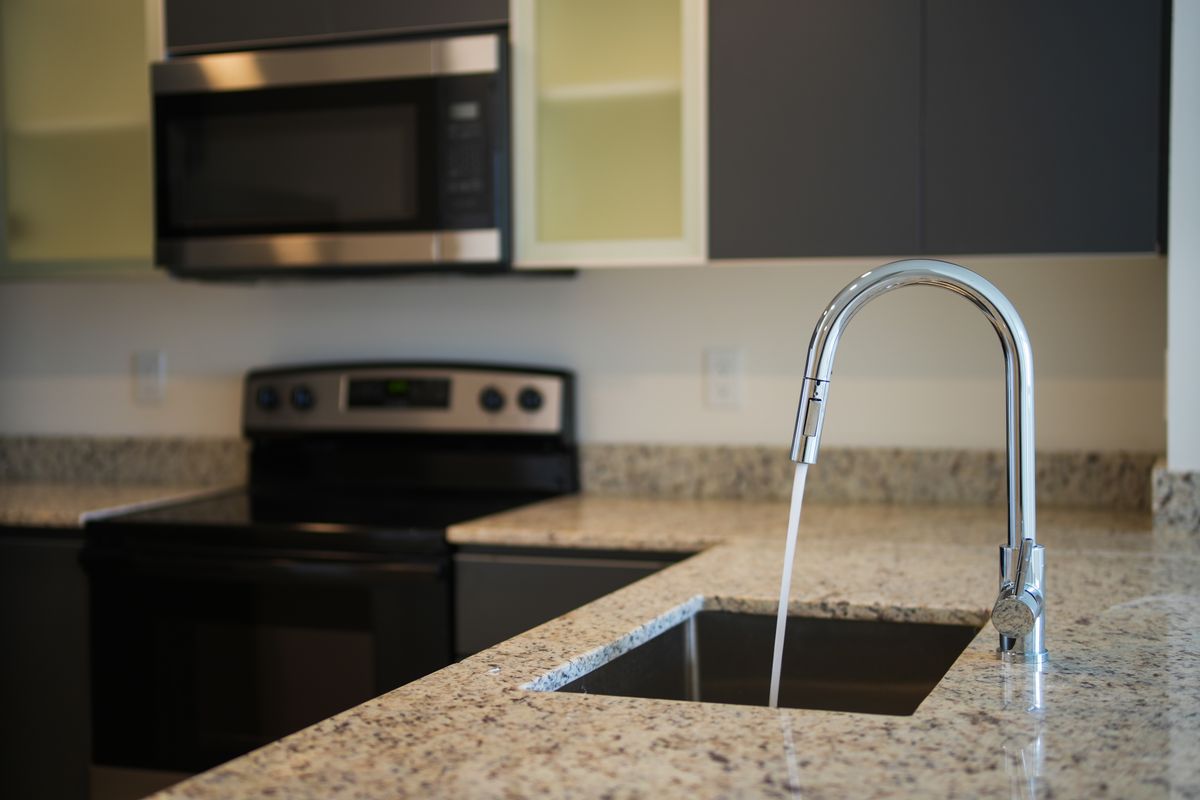 Kitchen with a chrome pull-down faucet running into an undermount sink set in a granite countertop, the cold line an under-sink RO system would tee into