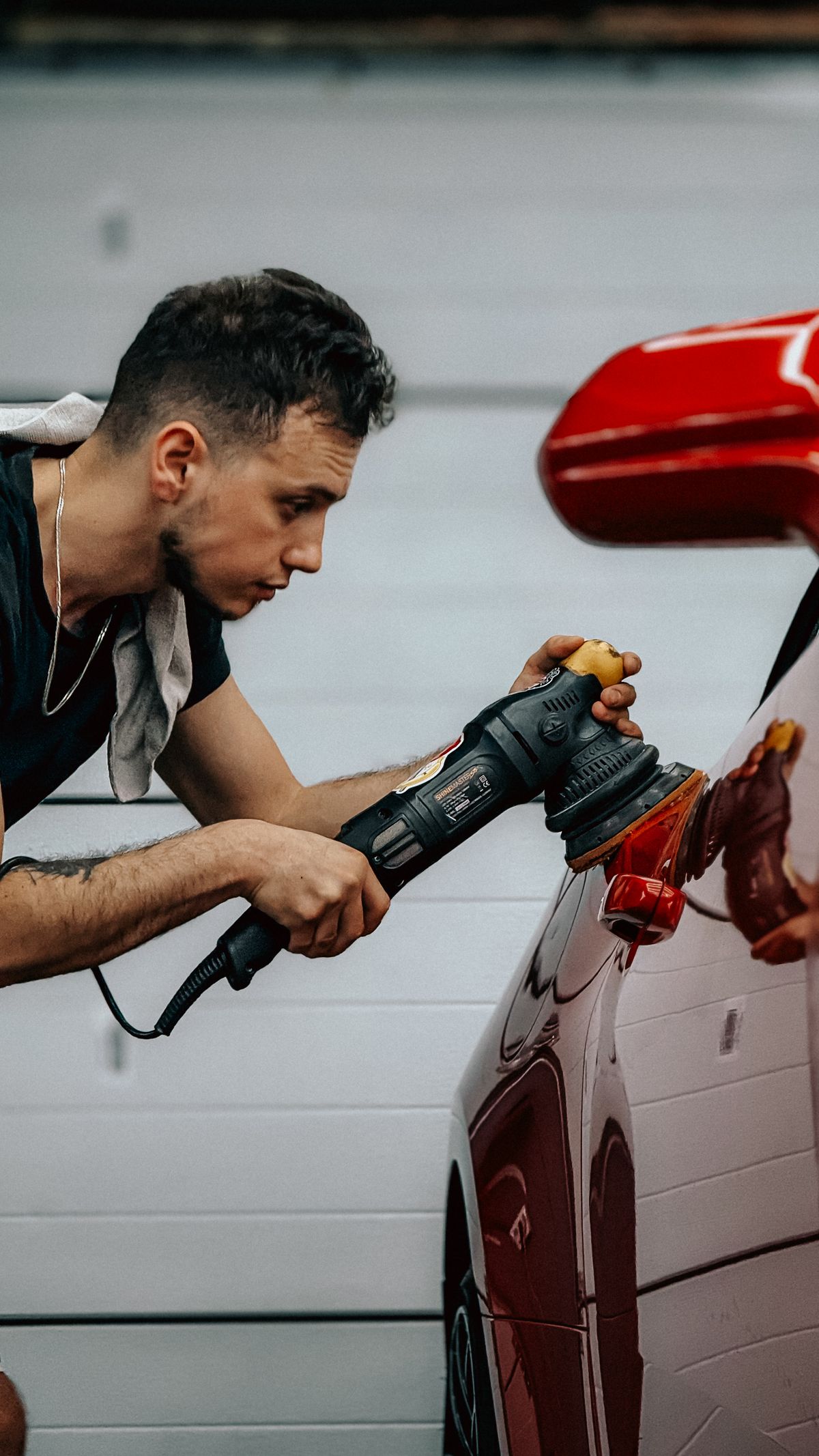 Man polishing a red car with an electric buffer in a garage to remove etched hard water spots from the clear coat