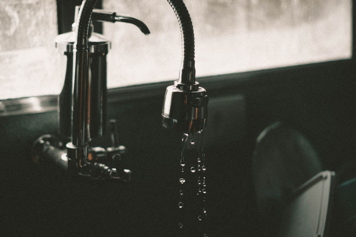 Water droplets falling from a chrome tap into a sink, the point at which black specks first become visible