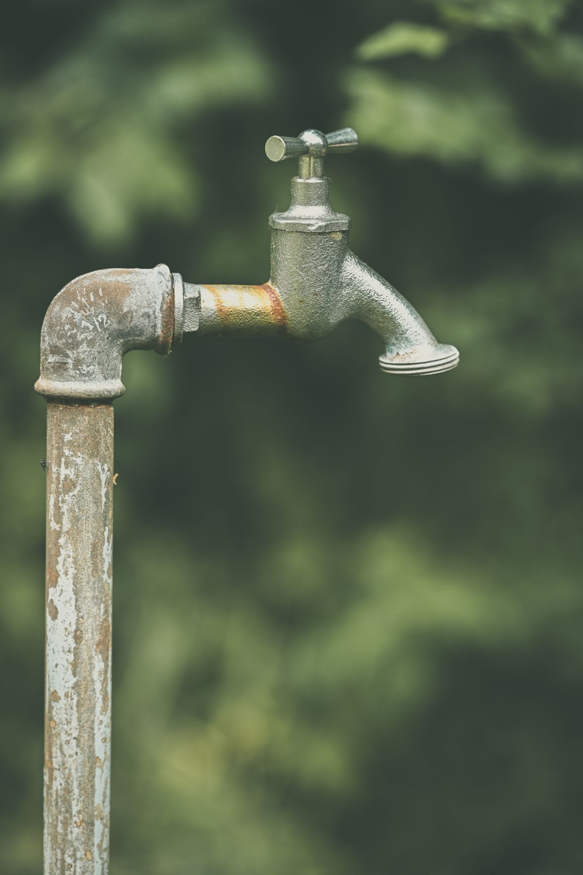Weathered outdoor faucet on a galvanized standpipe with an orange rust band at the joint, the oxidized iron a softener resin cannot exchange