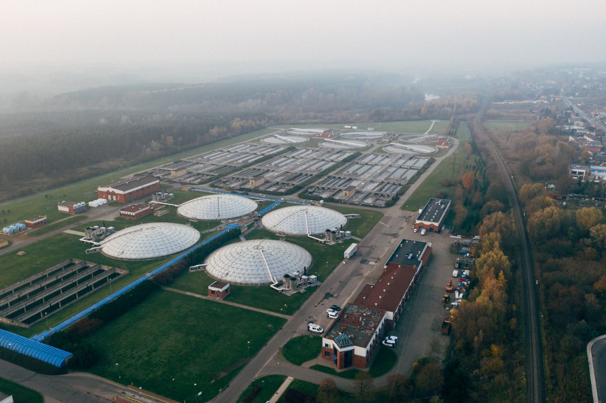 Aerial view of a large municipal wastewater treatment plant with domed tanks and rows of treatment basins beside a town