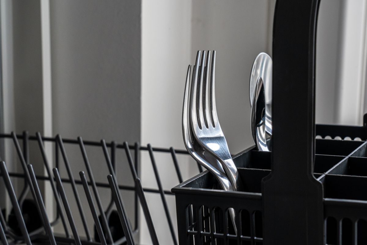 Stainless steel forks standing in a dishwasher cutlery rack after a wash cycle