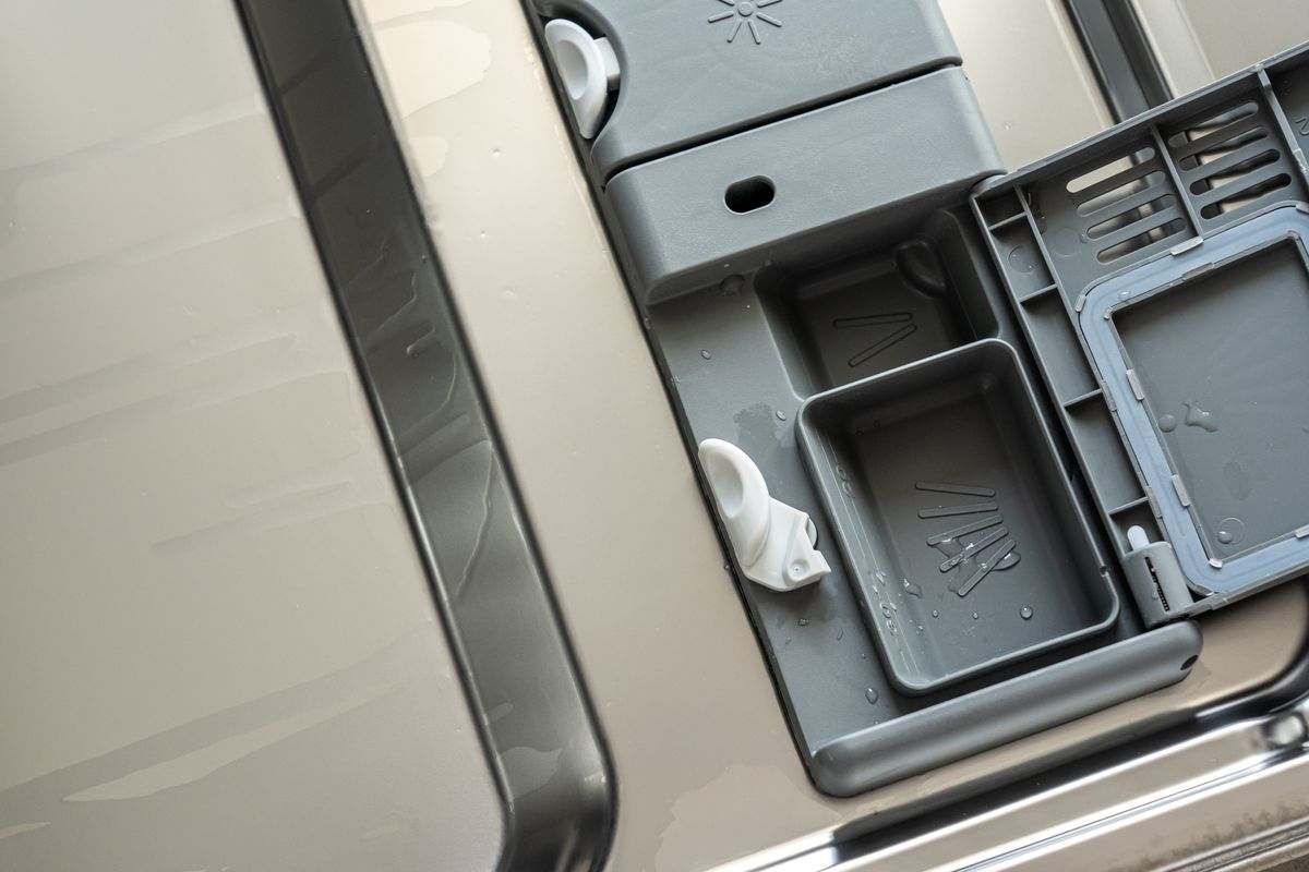 Close-up of an open dishwasher detergent dispenser compartment with water droplets