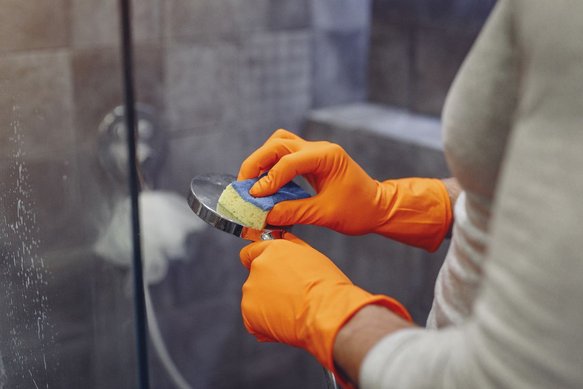 Gloved hand scrubbing mineral buildup from a shower fixture, showing how to remove white spots on faucets