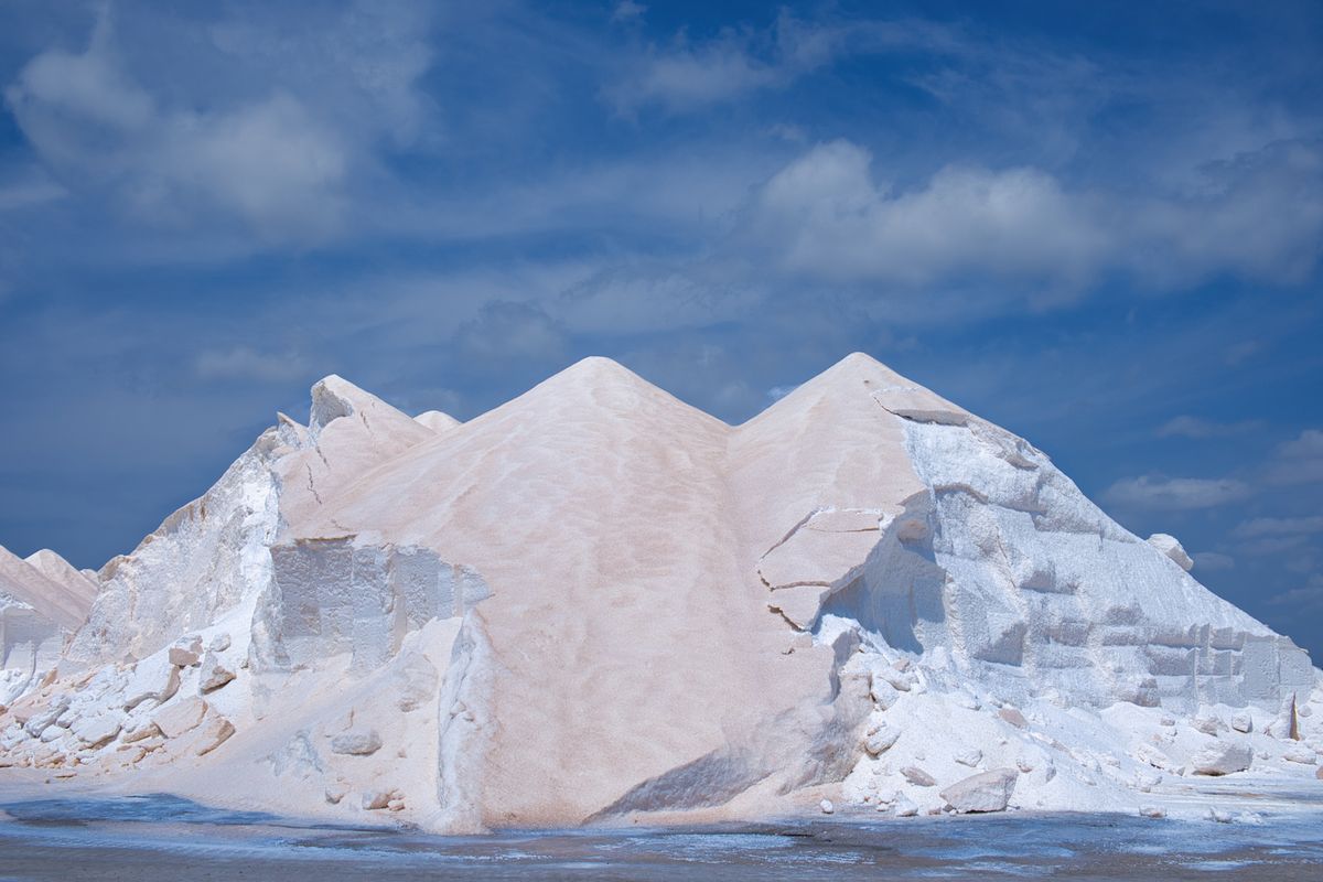 Large white stockpiles of harvested salt under a blue sky at an industrial salt production site