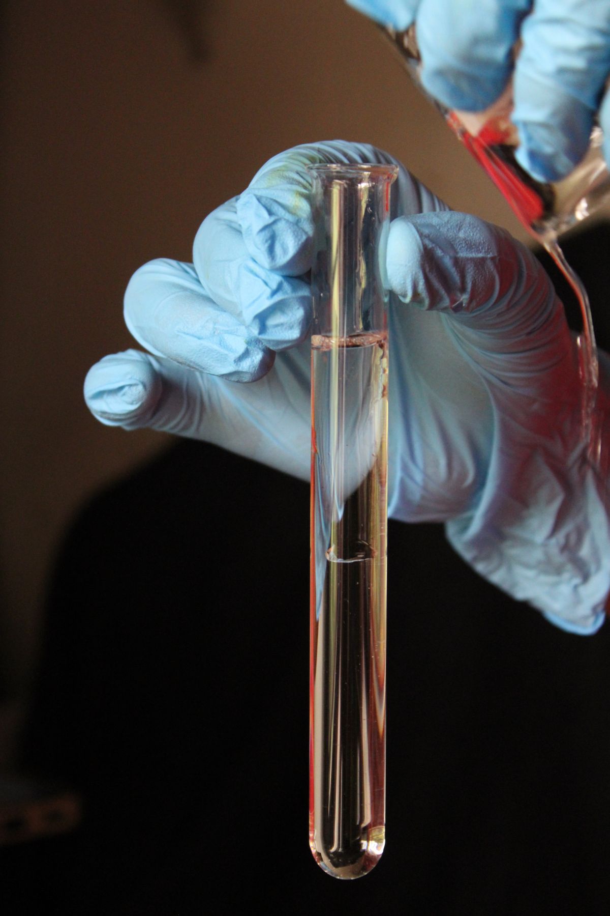 Gloved hand holding a clear water sample in a glass test tube in a laboratory