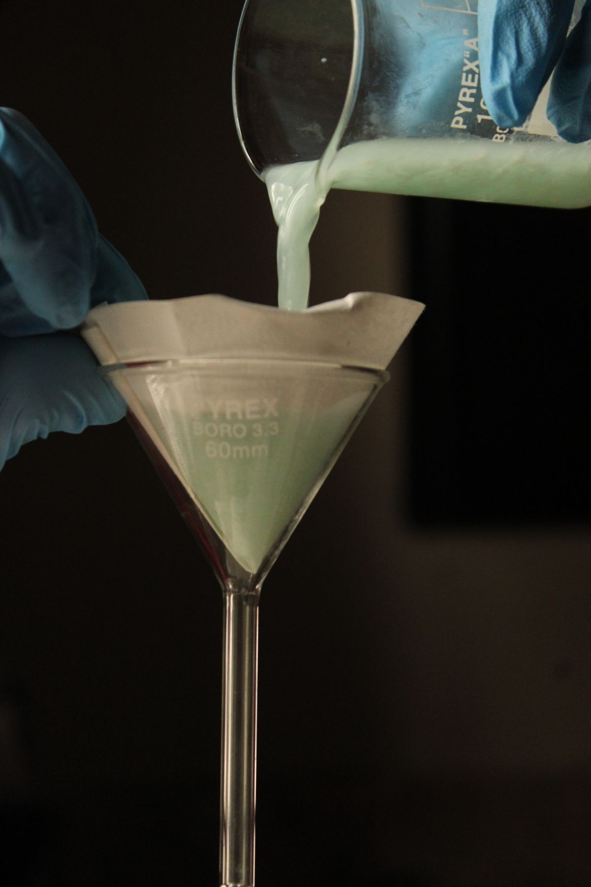 Liquid being filtered through paper in a laboratory funnel, the same separation a paper coffee filter performs on yellow well water