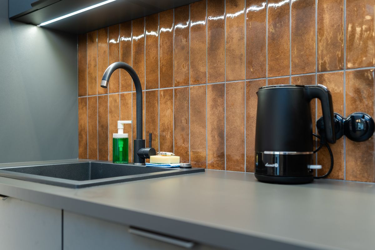 Black electric kettle beside a kitchen sink and mixer tap, set up to boil the same cold tap water before and after an electronic descaler is fitted