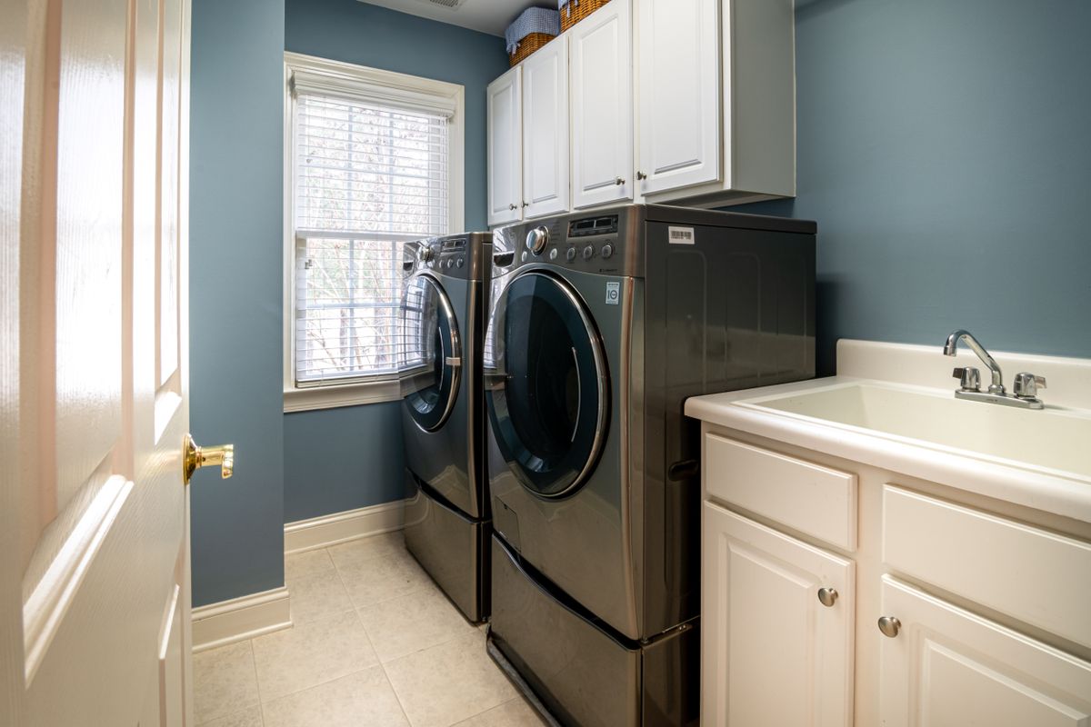 Laundry room with a front-loading washer and dryer, a utility sink and wall cabinets, an indoor room that can double as a water softener location