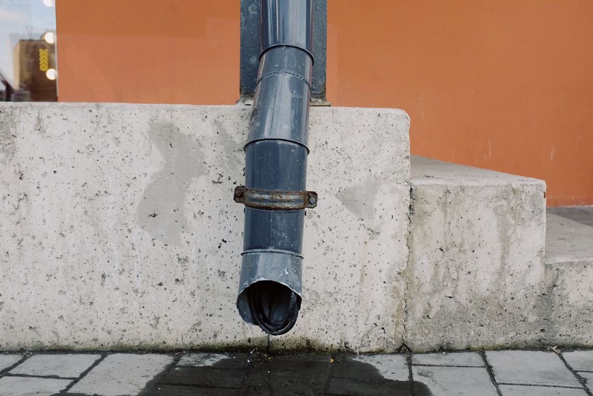Water dripping from the end of a drain spout, the kind of slow discharge-end drip that shows where a water softener drain line is leaking or overflowing