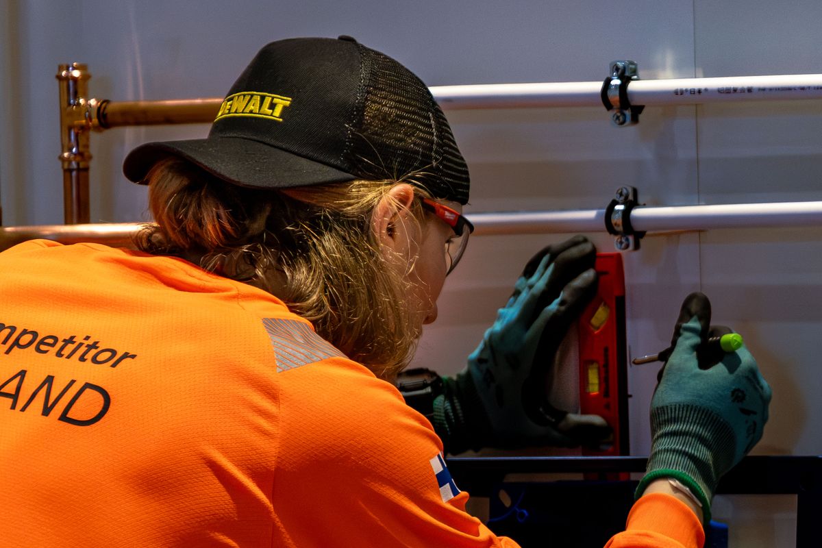 Installer in safety glasses and work gloves fitting wall-mounted copper and PEX water pipes during a plumbing installation