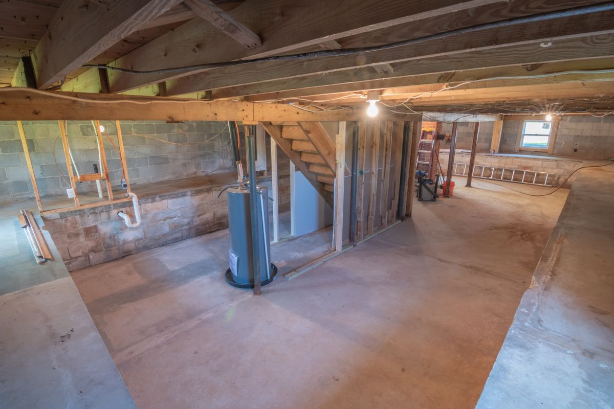 Empty basement interior with exposed beams and overhead plumbing pipes, the humid low-traffic space where most brine tanks sit and where bridging conditions develop