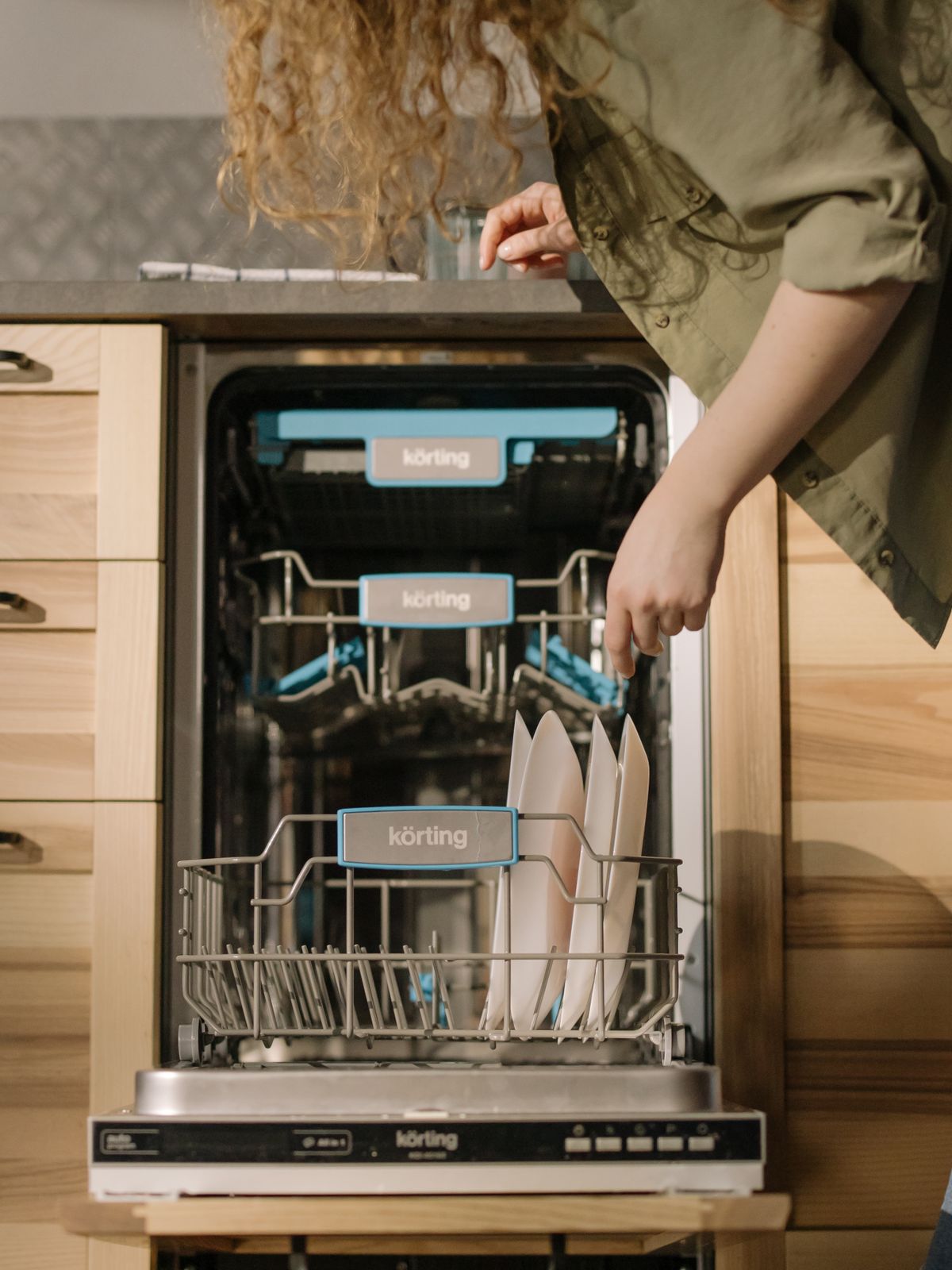 Hands loading dishes into an open dishwasher, the routine where detergent dose matters most after softening
