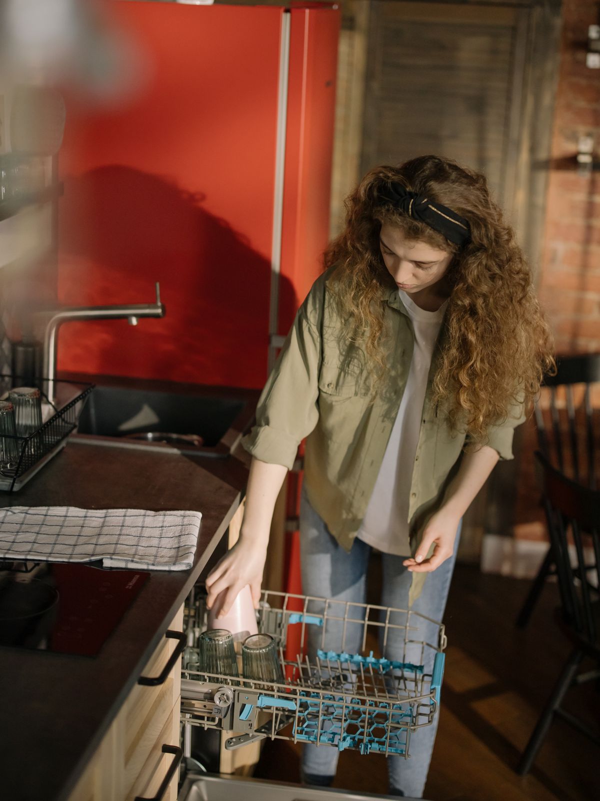 Person loading dishes into an open dishwasher in a sunlit kitchen