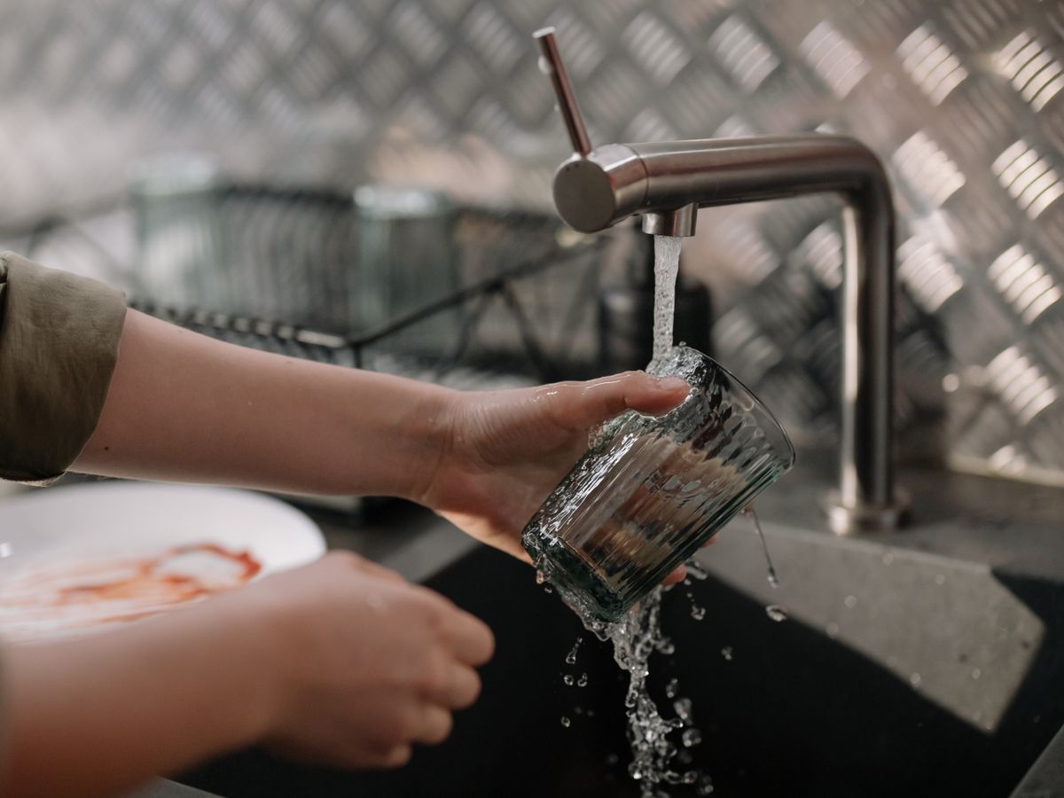 Person pouring tap water into a clear drinking glass to check for cloudiness and sediment