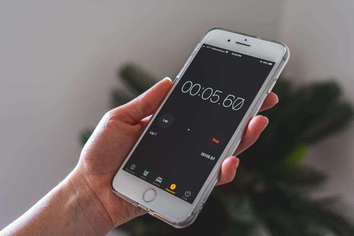 Hand holding a smartphone running a stopwatch app, the simple timing tool needed to measure how fast a softener drain line is flowing