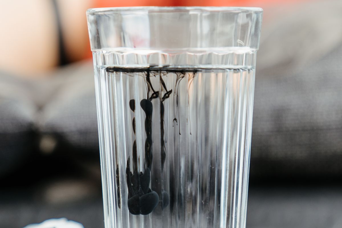 Dark ink dispersing through a clear glass of water, the same settling behaviour that reveals how much insoluble residue a salt grade leaves behind