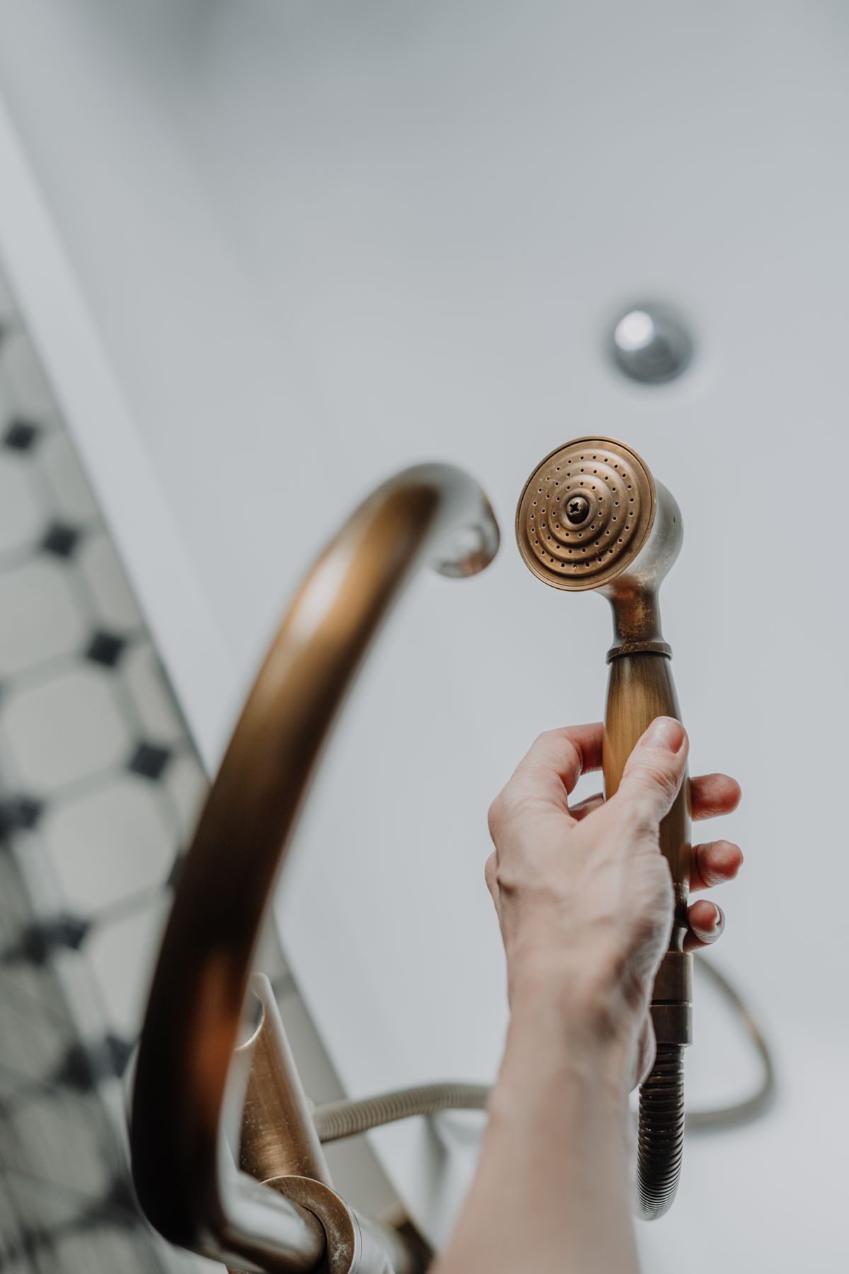 Person holding a detached brass shower head in a modern bathroom
