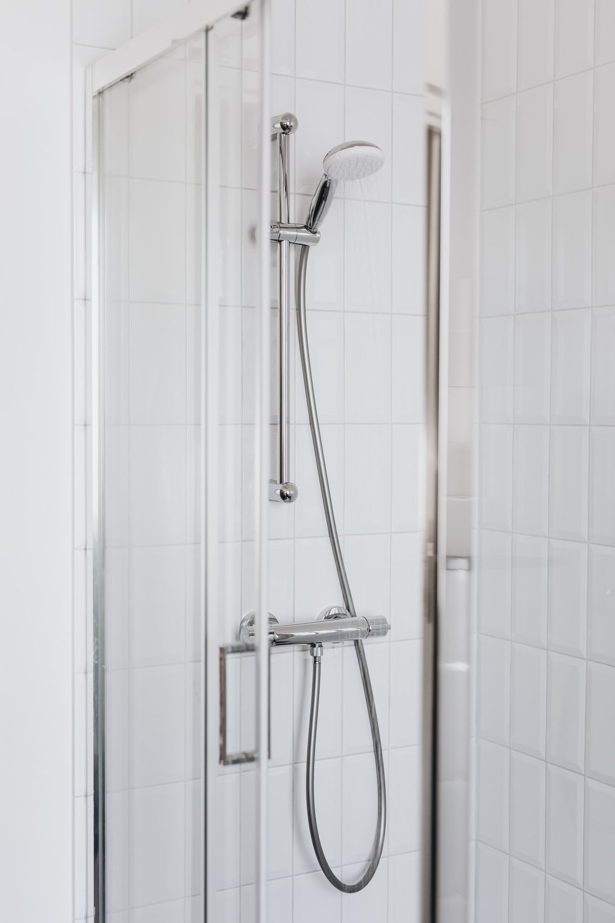 Handheld showerhead on a slide bar inside a glass-walled shower with white tiles