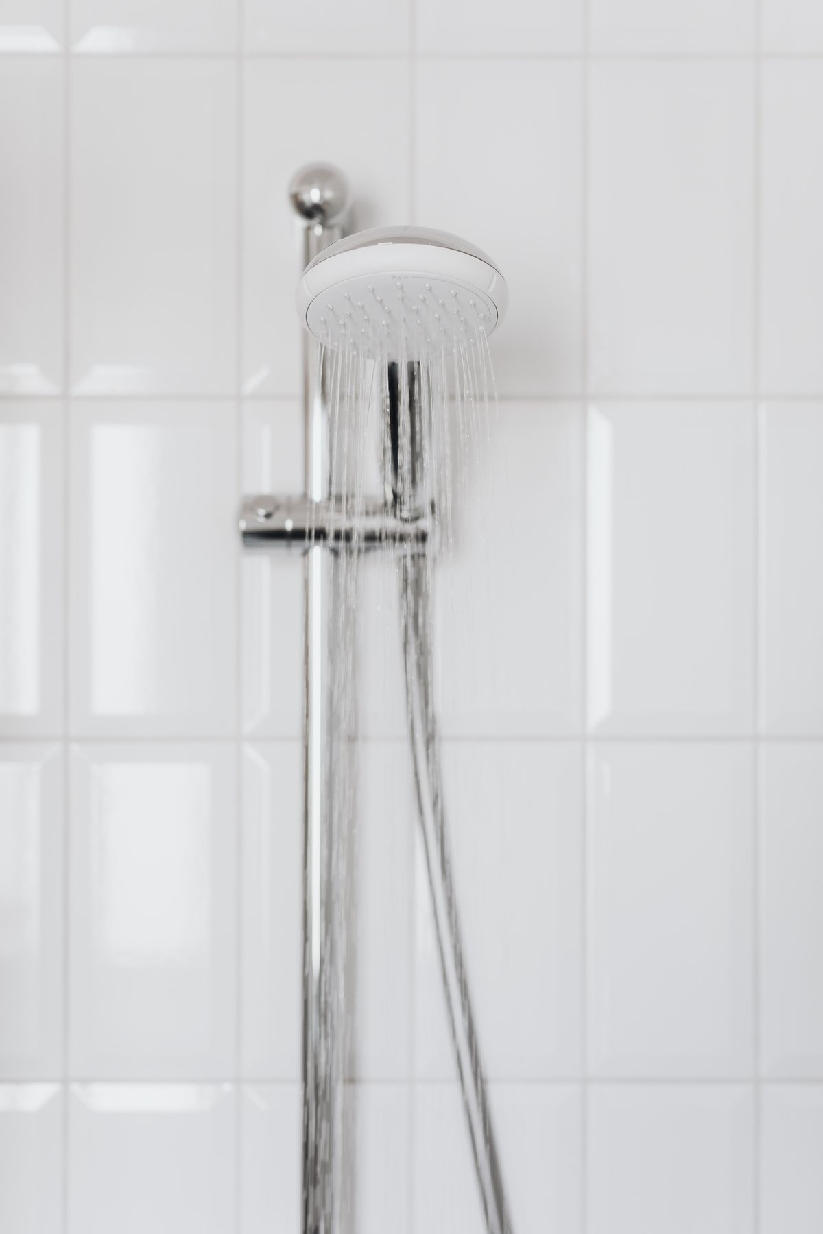Chrome showerhead with water flowing against white tile, the daily point of comparison where the change in feel is most noticeable