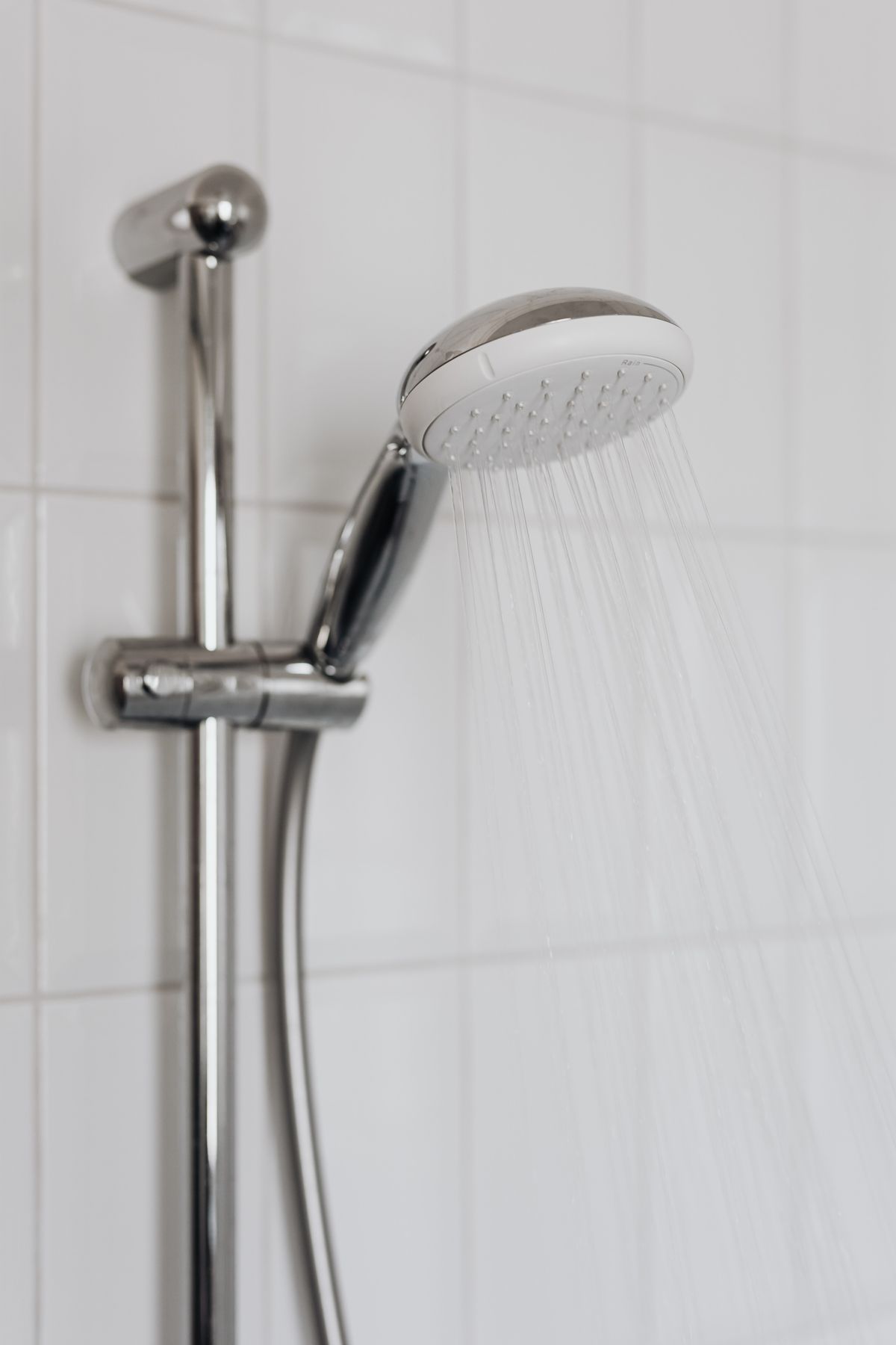 Chrome shower head with water flowing in a tiled bathroom