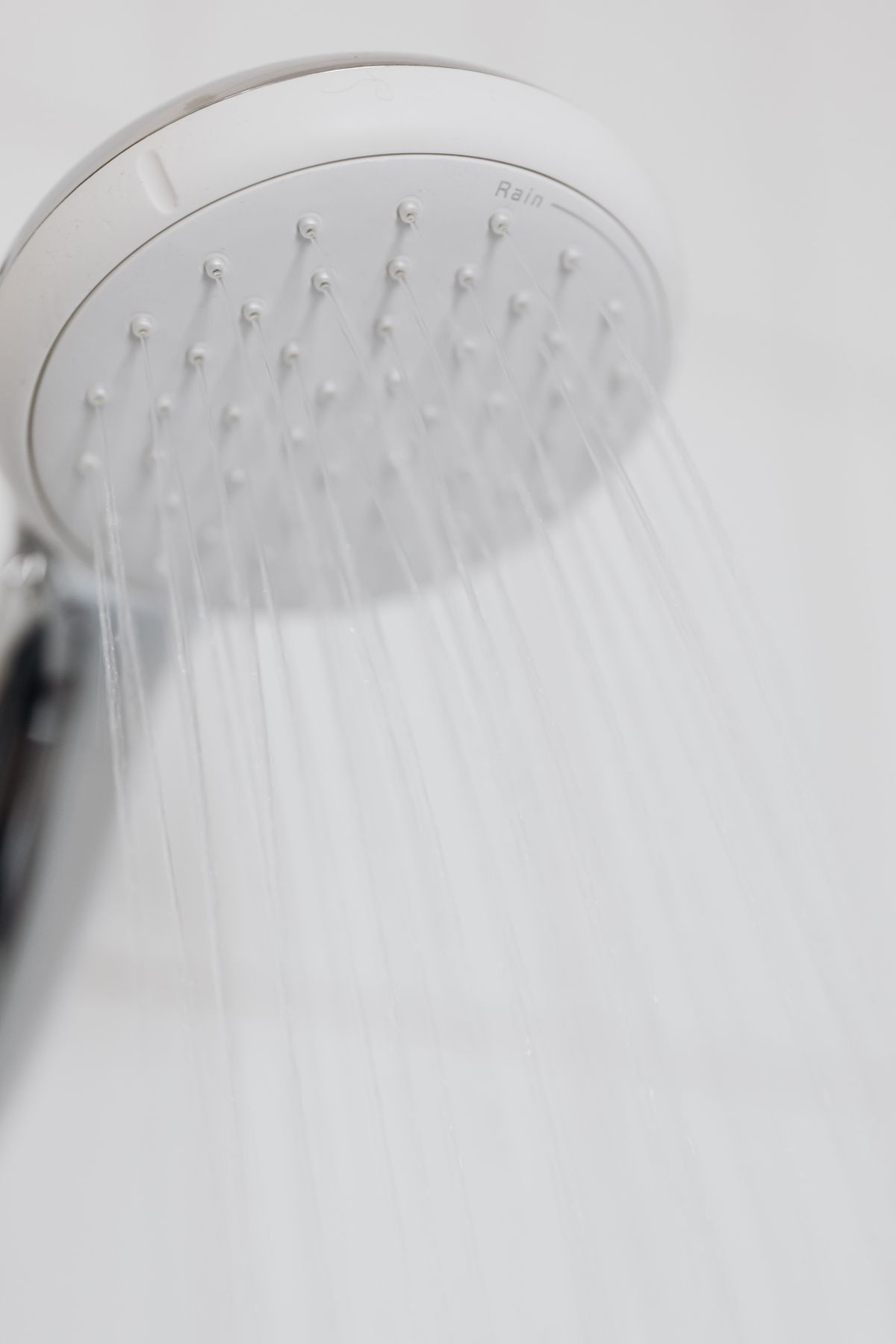Modern chrome shower head running water in a white bathroom before a hard water clogged showerhead descale