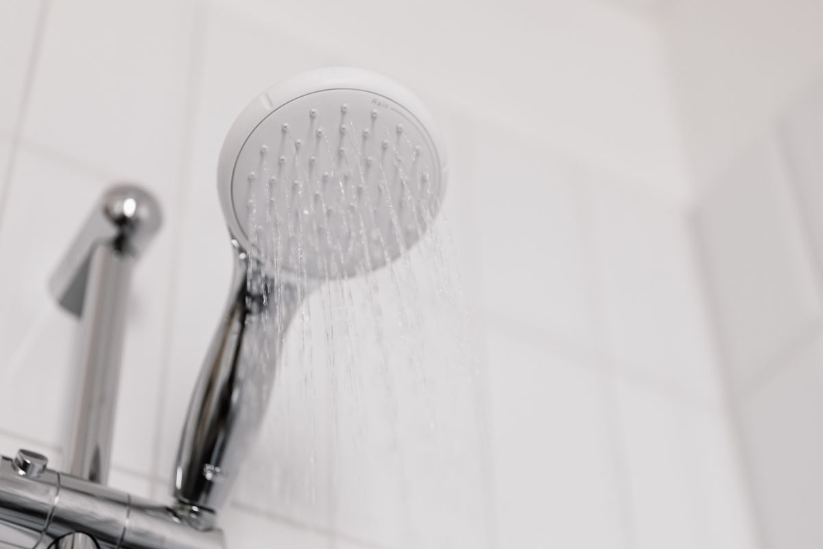 Chrome shower head running water in a tiled bathroom, illustrating what is hard water in everyday household use