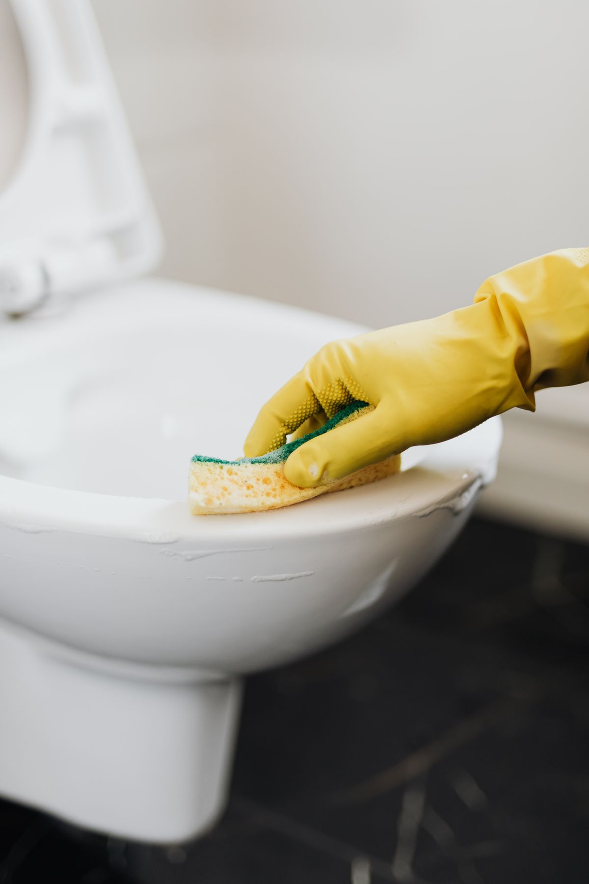 Gloved hand scrubbing the rim of a white toilet bowl with a sponge, the chore that black manganese staining from well water makes a weekly job