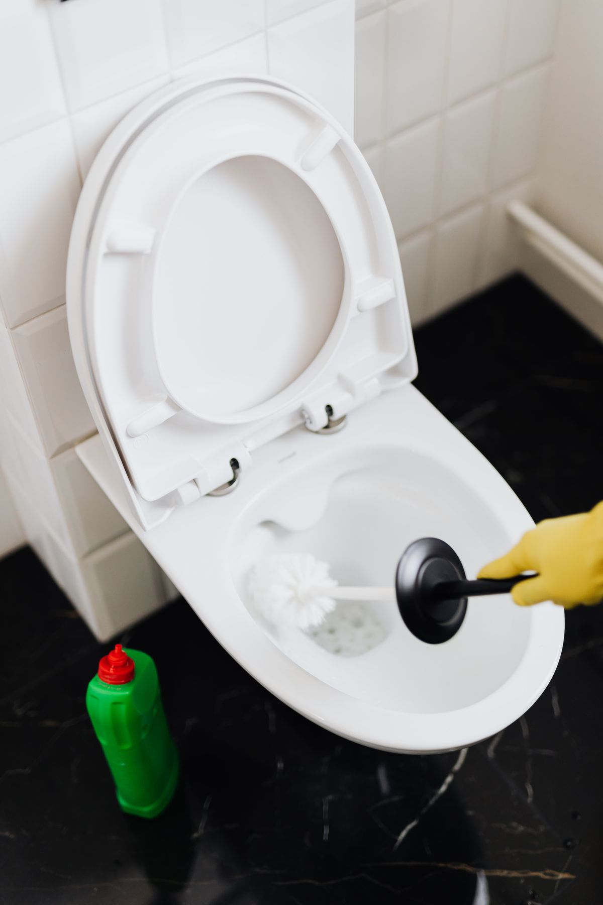 Gloved hand scrubbing a hard water ring in the toilet bowl at the waterline with a brush