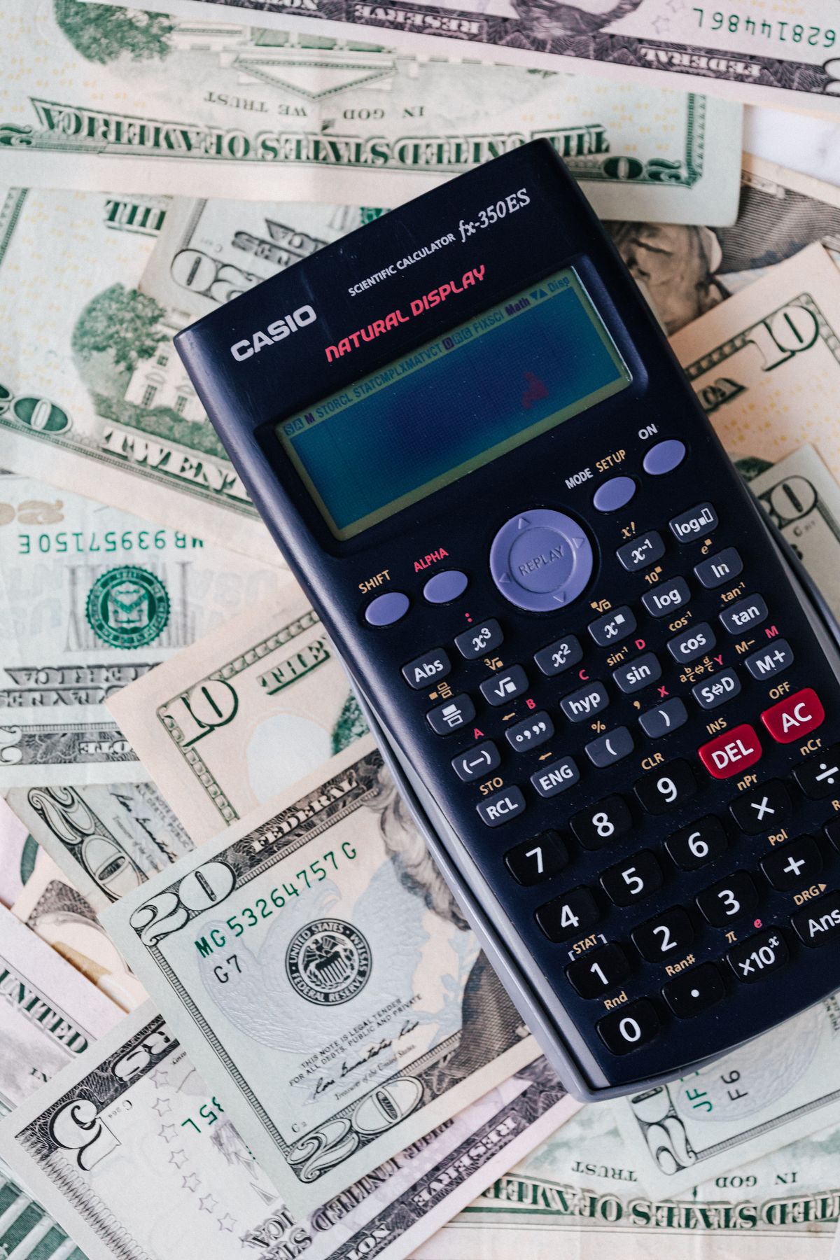 Electronic calculator lying on a spread of US dollar bills, used to total ten years of salt-free conditioner cartridges against a softener's salt