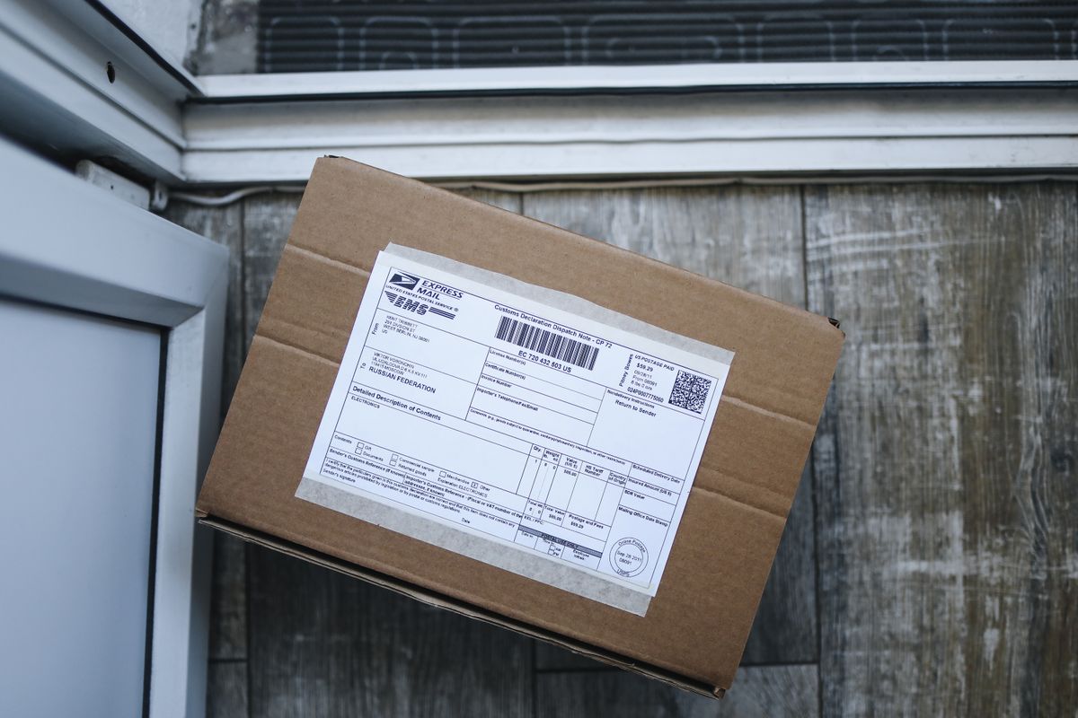 Brown cardboard parcel with a shipping label on a wooden floor just inside a front door, how an online-only softener arrives for DIY installation