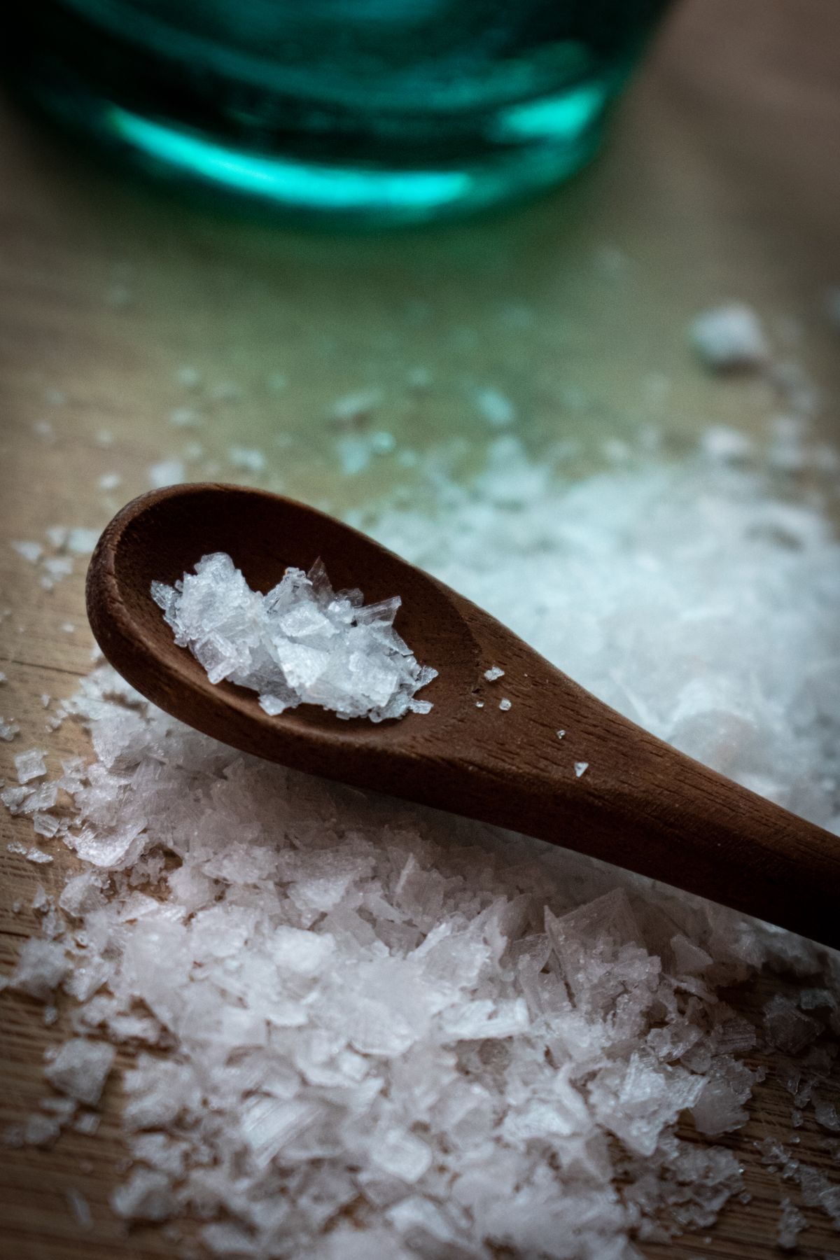 Wooden spoon holding a measured portion of coarse white salt crystals on a wooden board