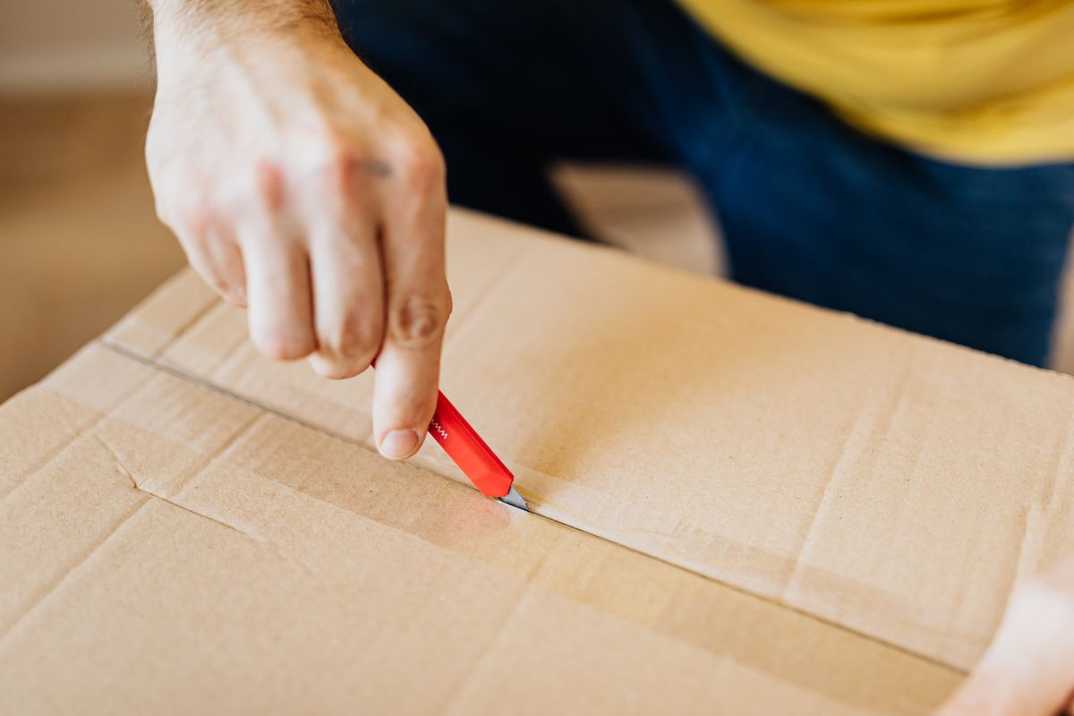 Person slitting the tape on a large cardboard shipping box with a red utility knife, the moment to check an online water softener's box contents against the listing