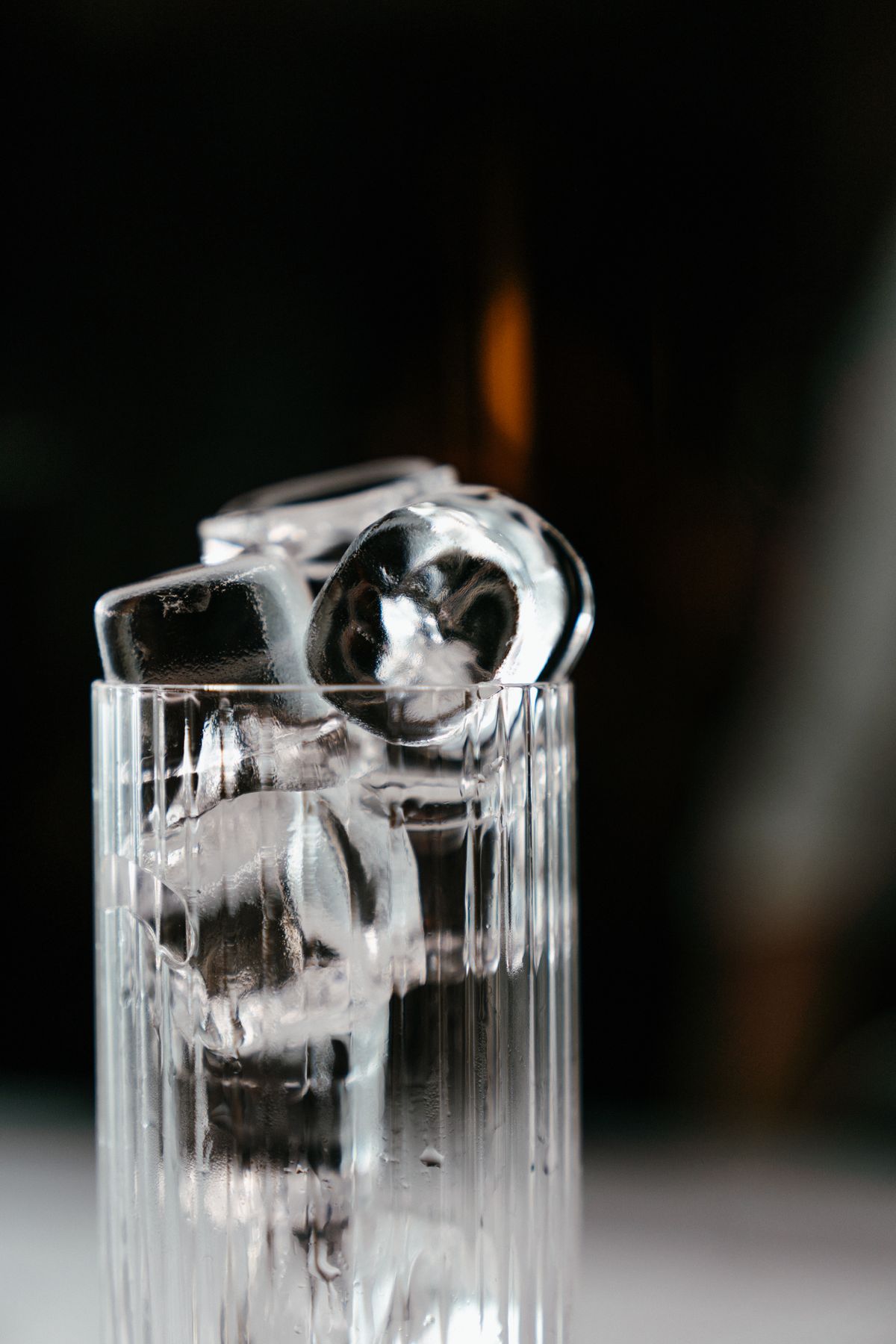 Clear ice cubes stacked in a glass against a dark background