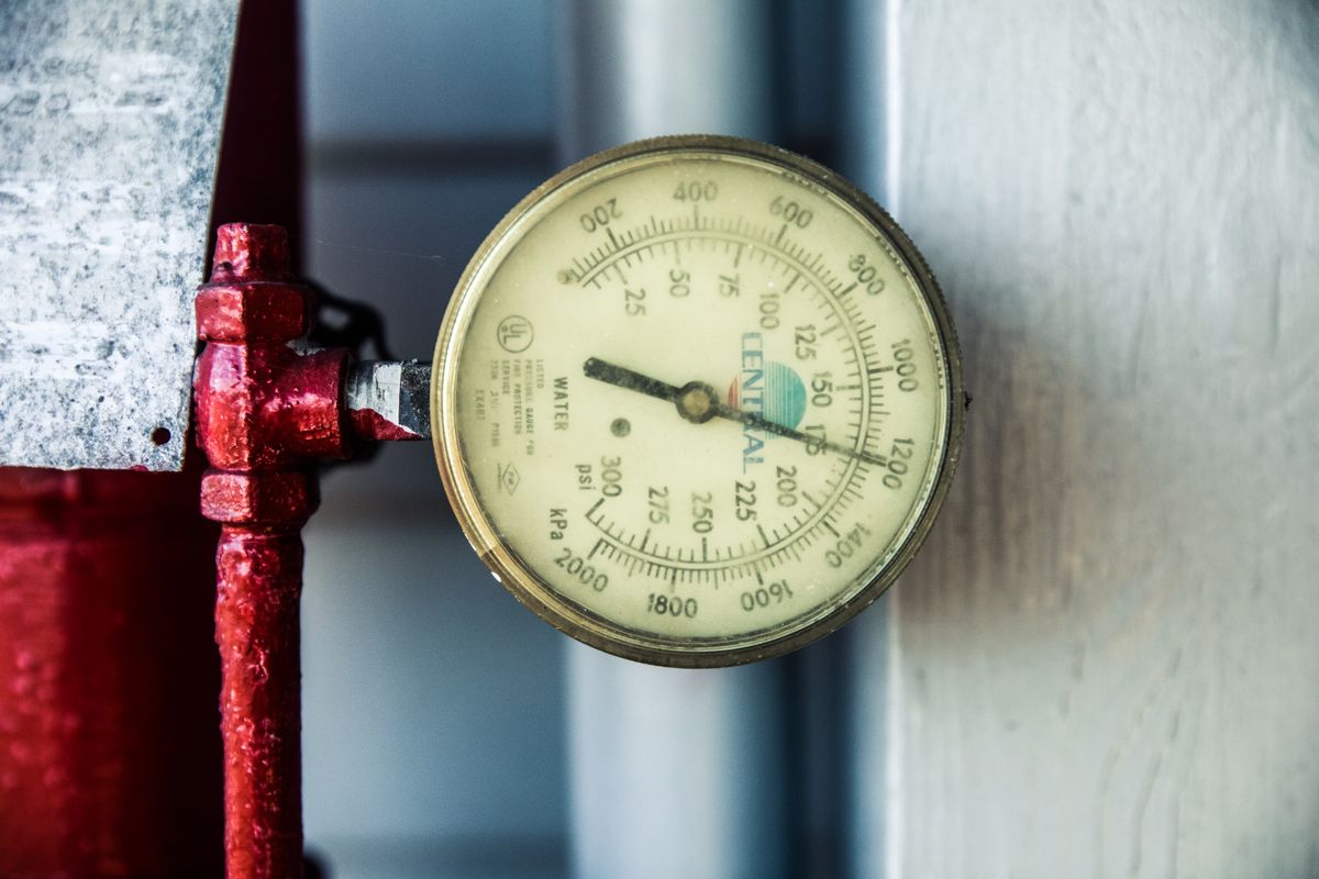 Close-up of a pressure gauge fitted to a red industrial pipe, the reading to watch when a pressure-reducing valve is failing or set too high