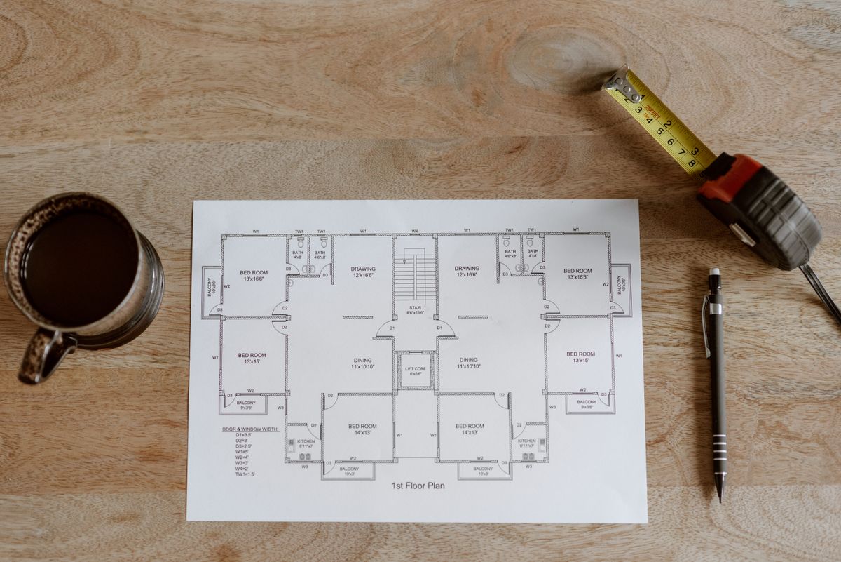 Printed house floor plan on a wooden table with a tape measure and pencil, used to map hardness test results fixture by fixture