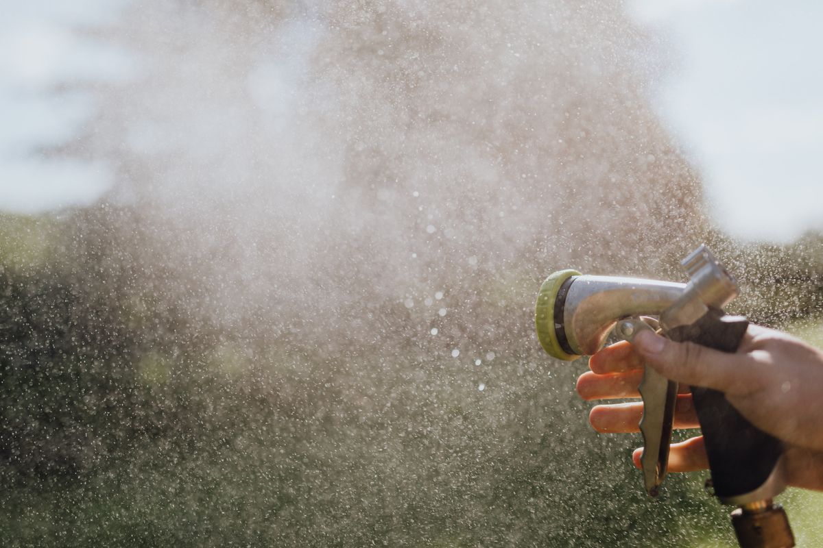 Hand holding a garden hose spray nozzle misting water, the same narrowing-orifice effect that speeds up water inside a water softener injector venturi