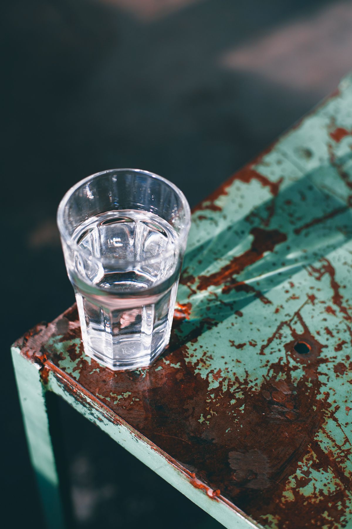 High-angle view of a glass of cold water on a worn surface, the first-draw sample used to test for metal picked up from plumbing