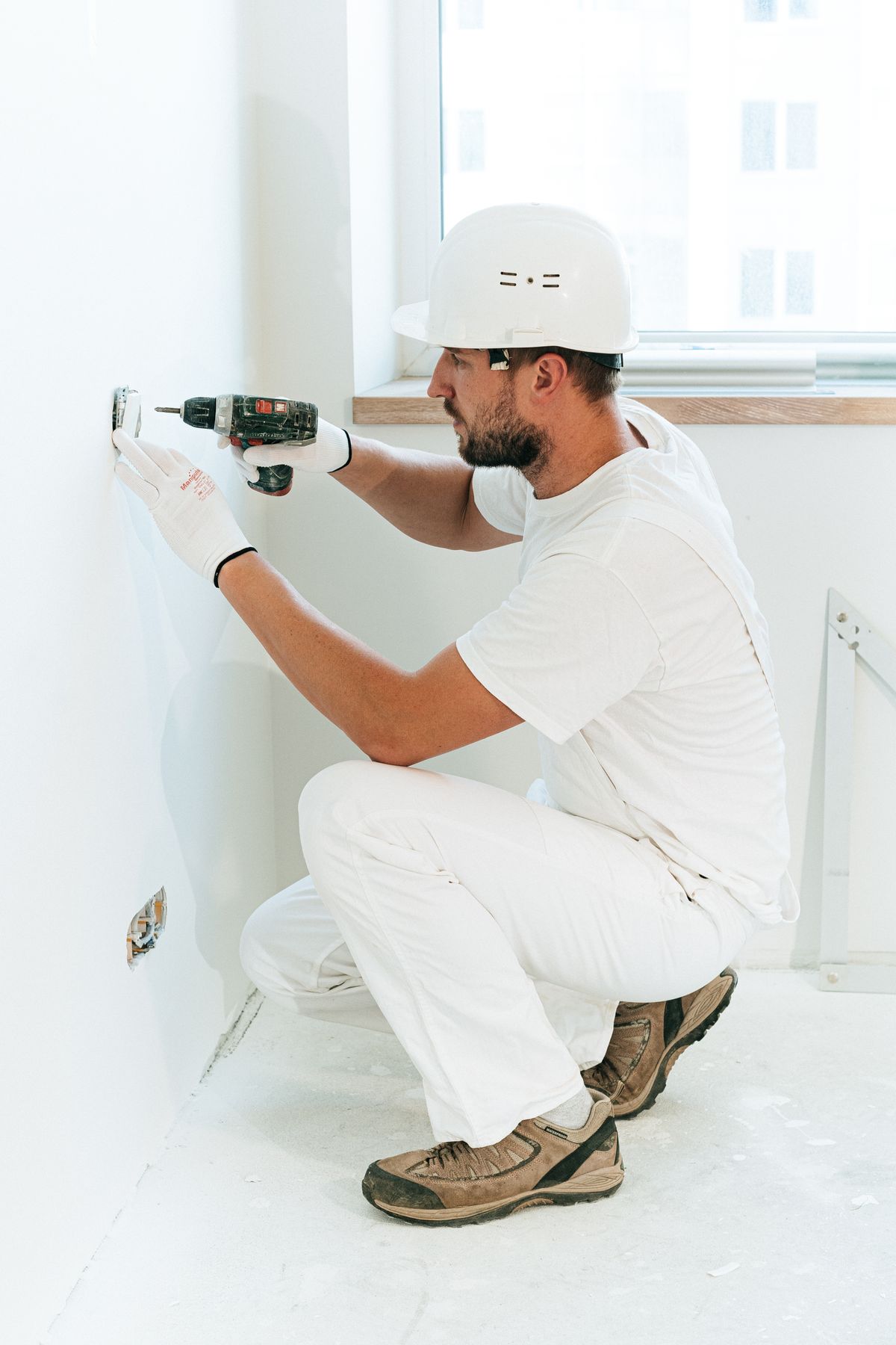 Installer kneeling to fit a new electrical outlet in a wall, the line item a full softener reinstall pays for and a like-for-like swap usually reuses