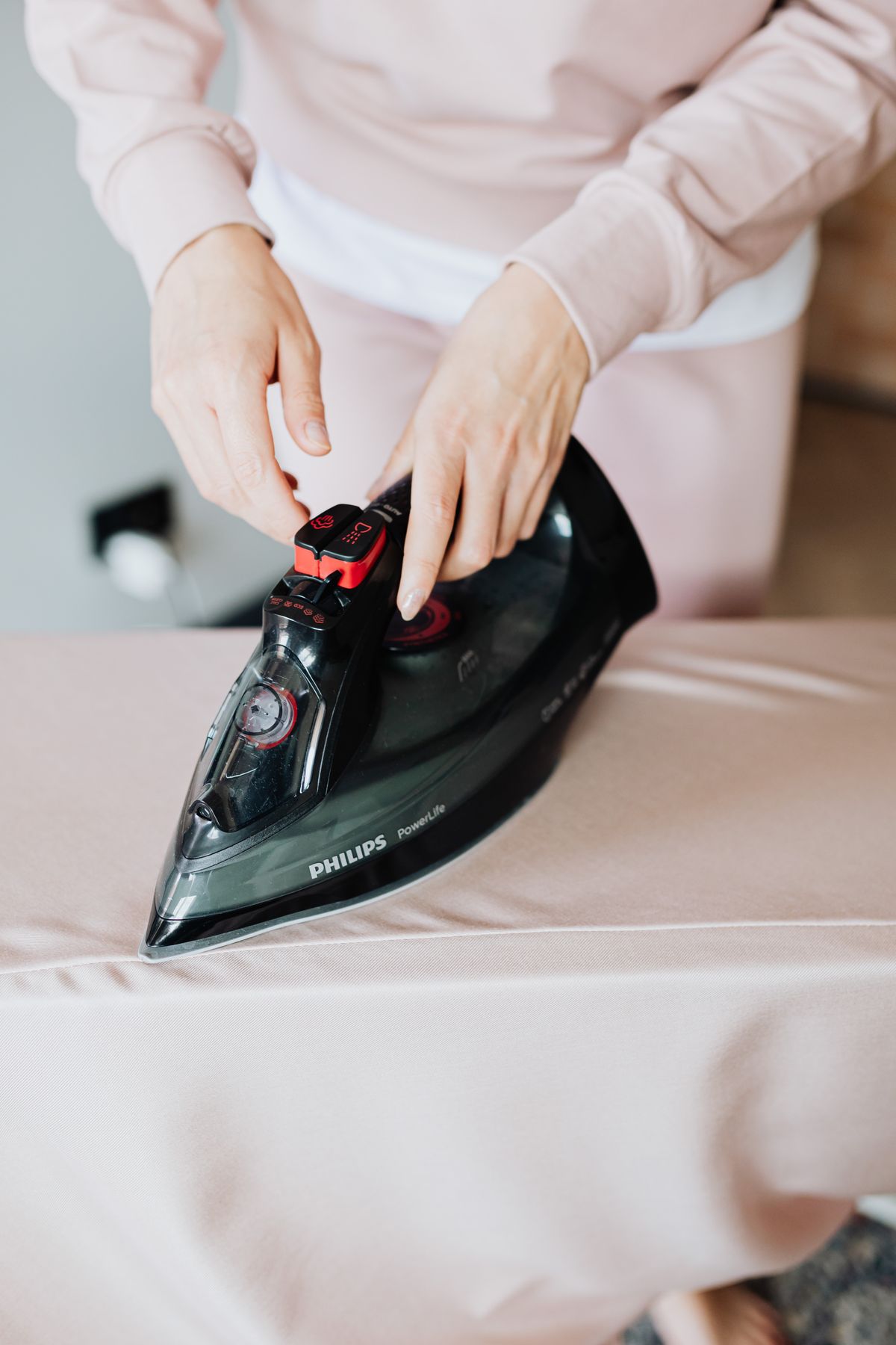 Person pressing fabric with a black steam iron on an ironing board, an appliance where softened water rules vary by maker