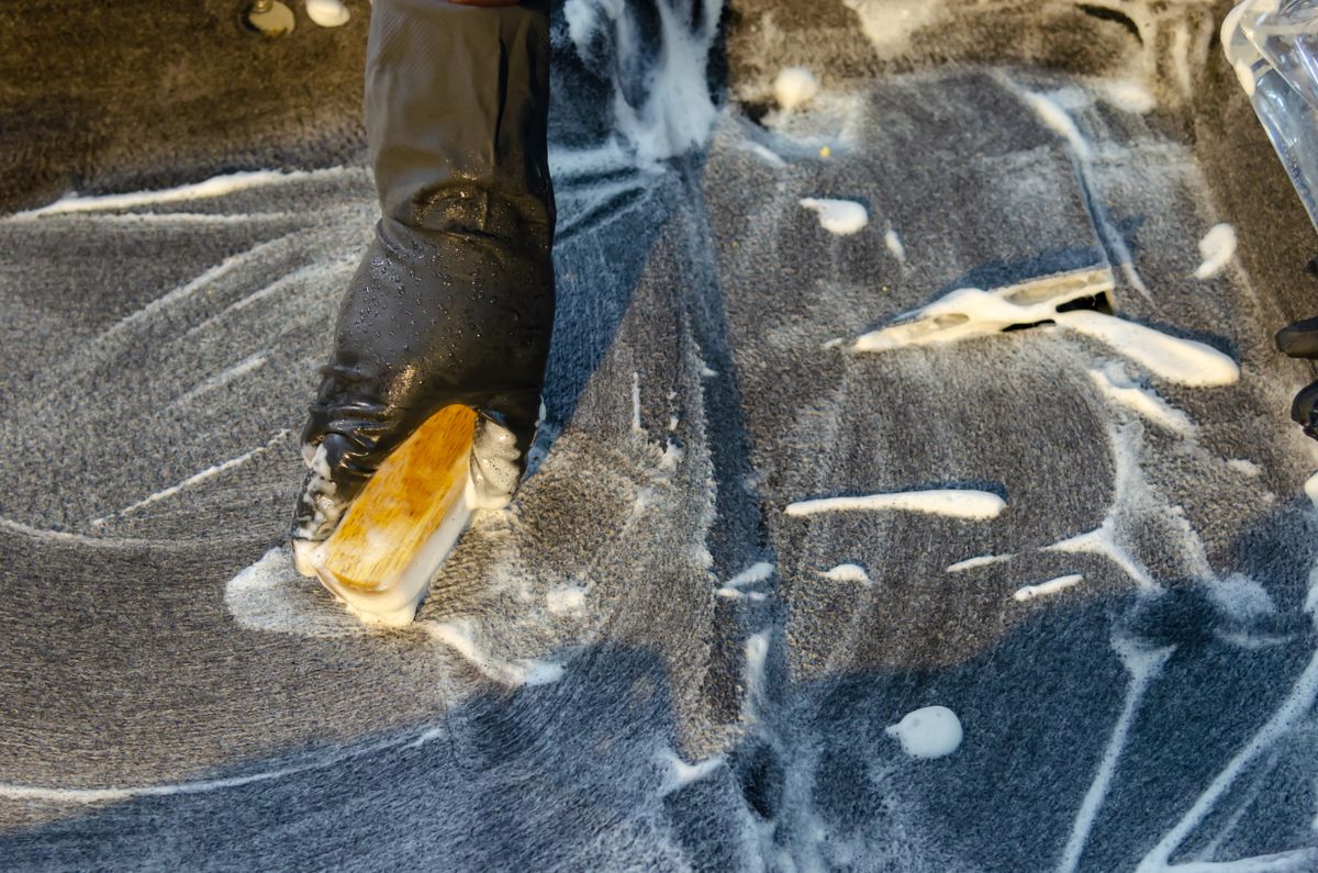 Gloved hand applying detergent with a cleaning brush to a surface, the final wash before a brine tank is rinsed and reassembled