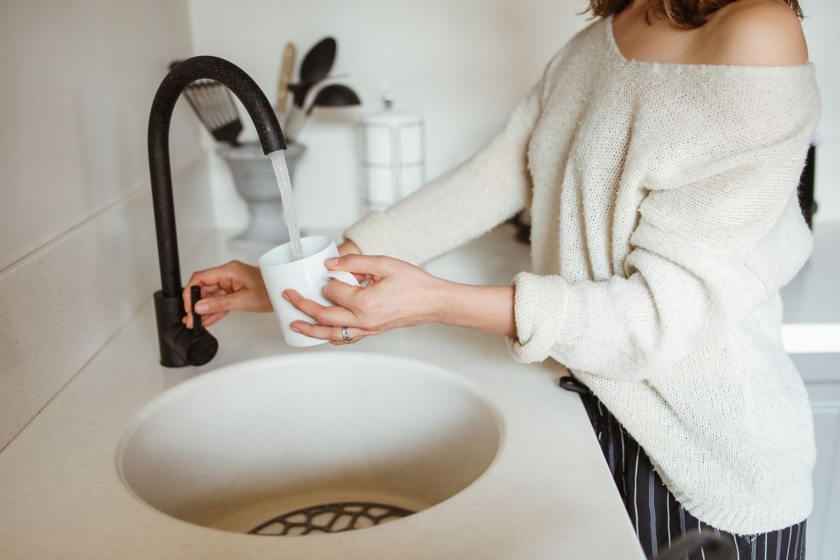 Woman filling a white mug from a black kitchen faucet, the single tap a point-of-use drinking water system serves