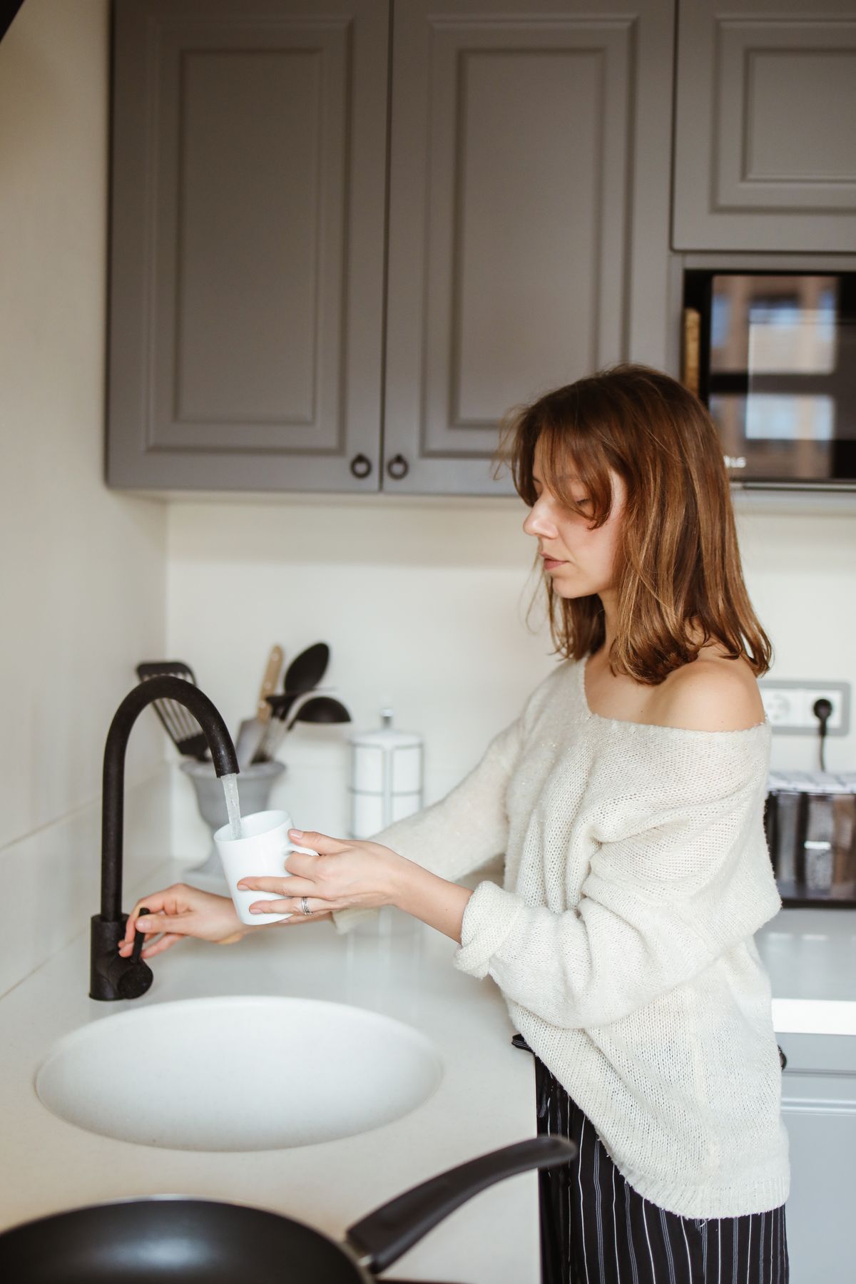 Filling a mug from a kitchen faucet, the sampling step in the seven-day hot-versus-cold hardness comparison