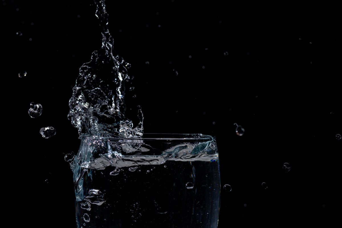 Water splashing into a glass against a dark background, showing the entrained air that makes freshly drawn water look milky